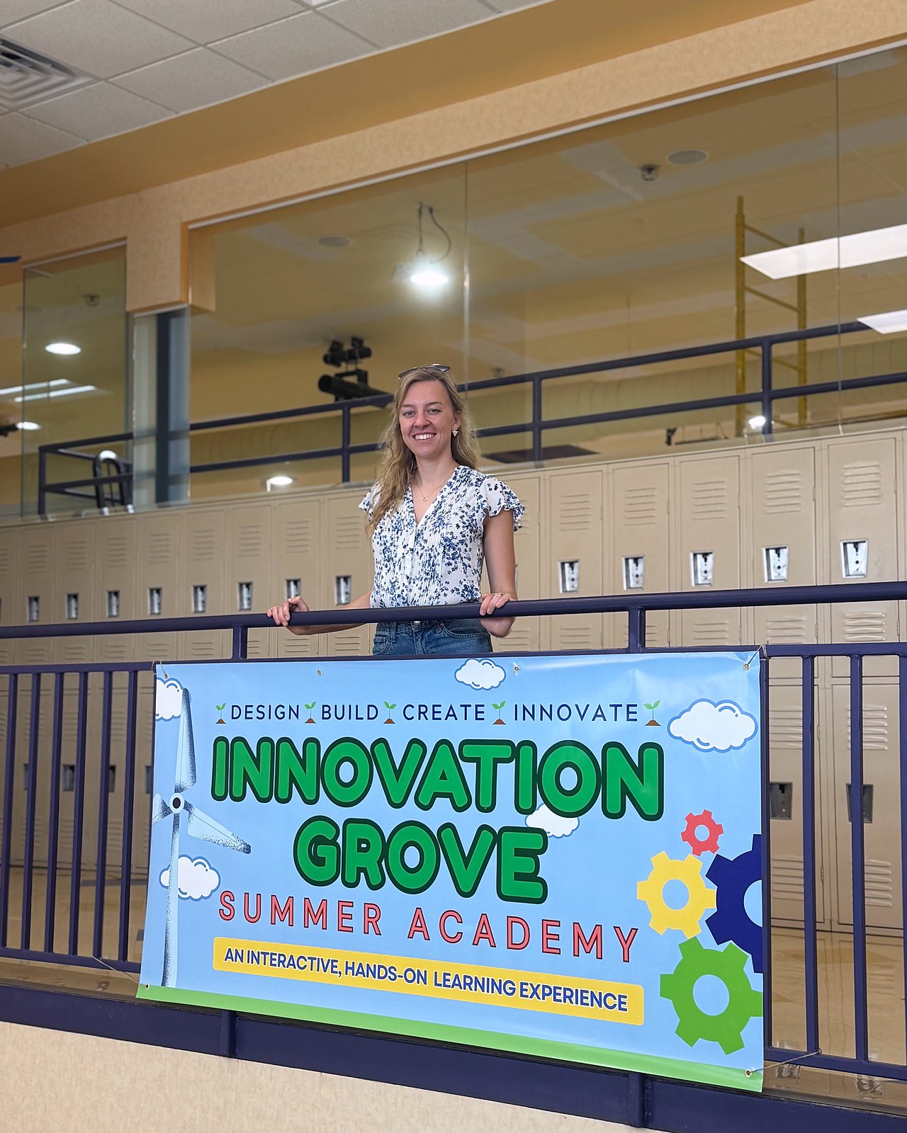 Dr. Loretta Sutkus at a balcony railing inside Next Generation School, with the Innovation Grove Summer Academy banner hung below her