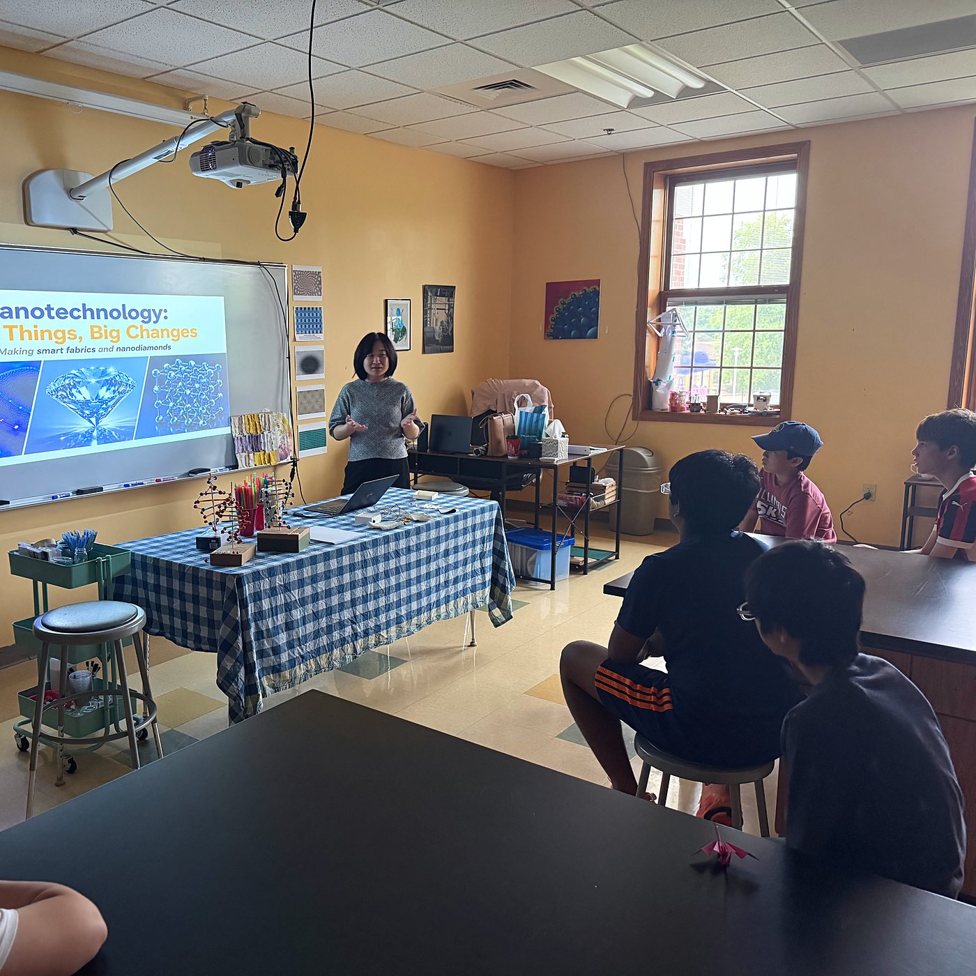 A guest speaker mid sentence beside her nanotechnology slide, students watching from the tables