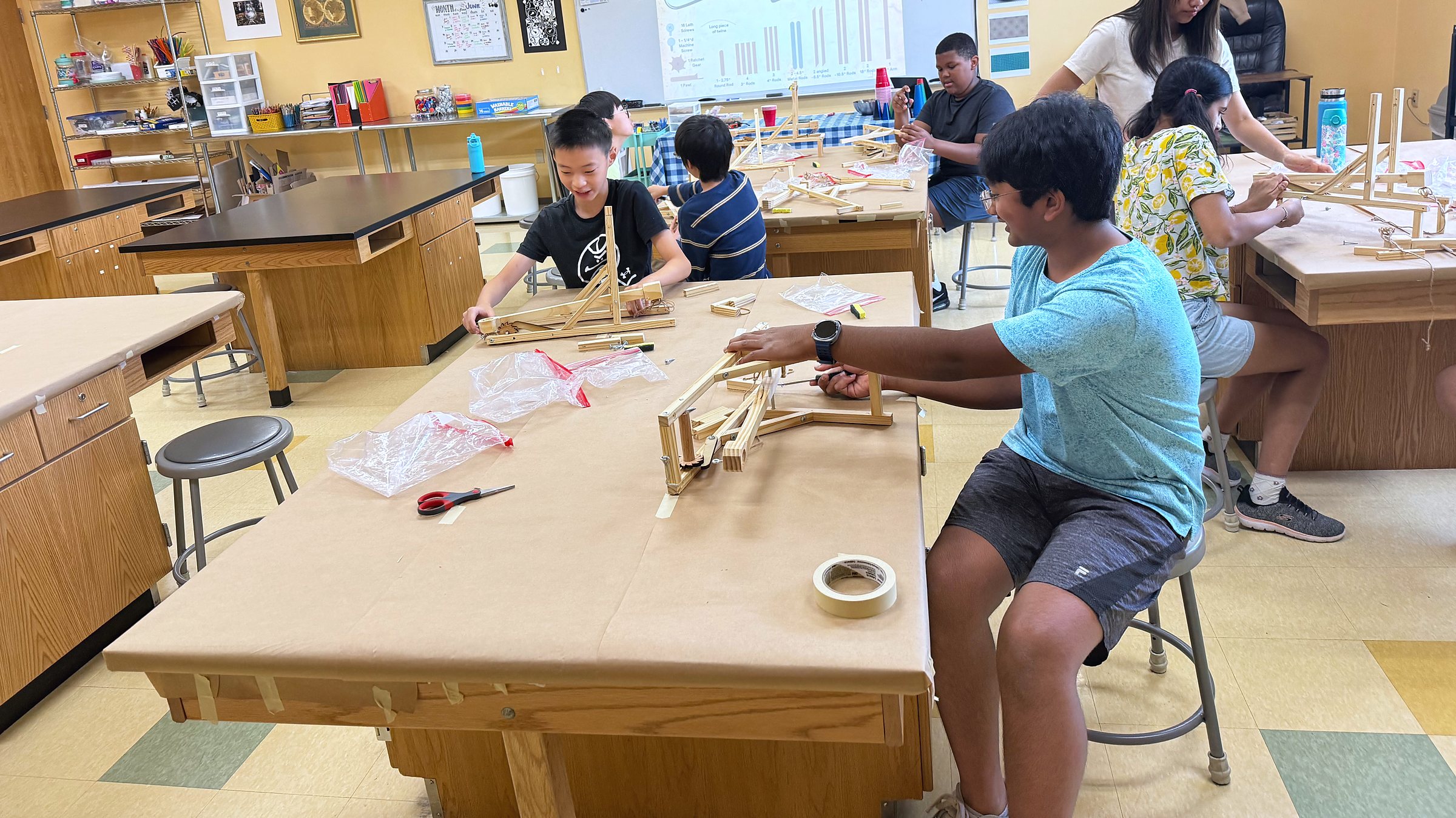 The academy classroom in full swing, students at the work tables building catapults