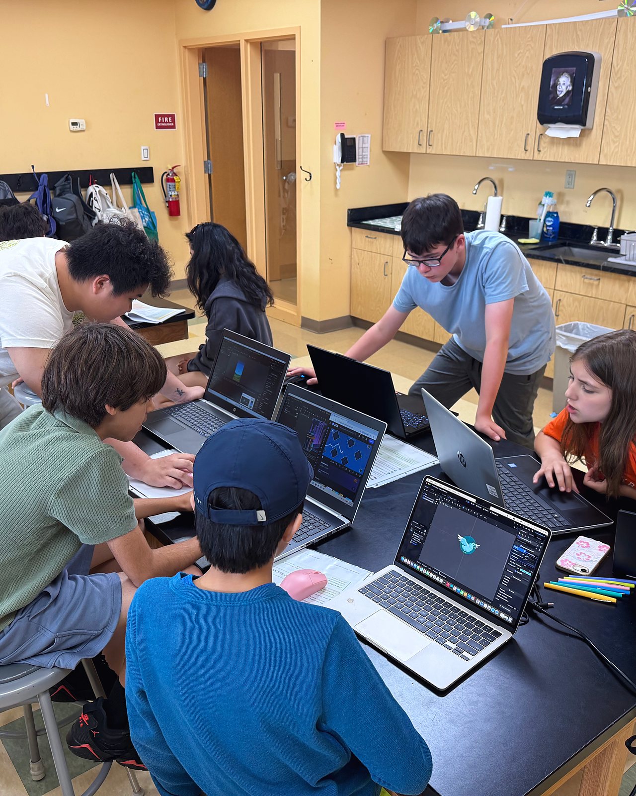 Students at laptops building their games in Unity while an instructor leans over to help