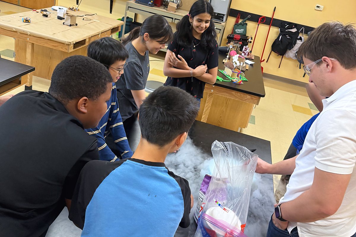 A guest scientist runs a cryogenics demo at the front table while students lean in through the fog