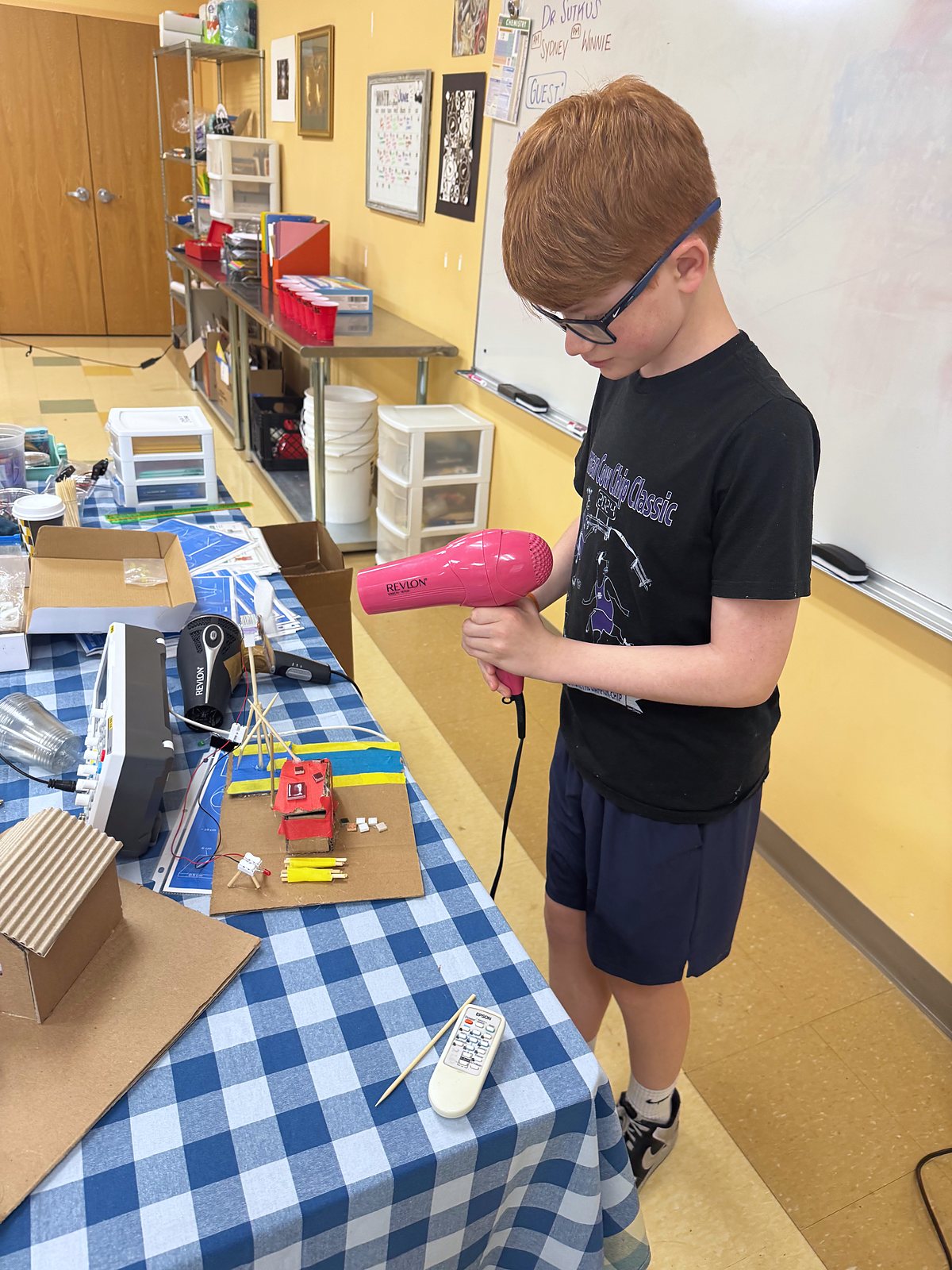 A student tests the wind turbine on his cardboard house with a hair dryer
