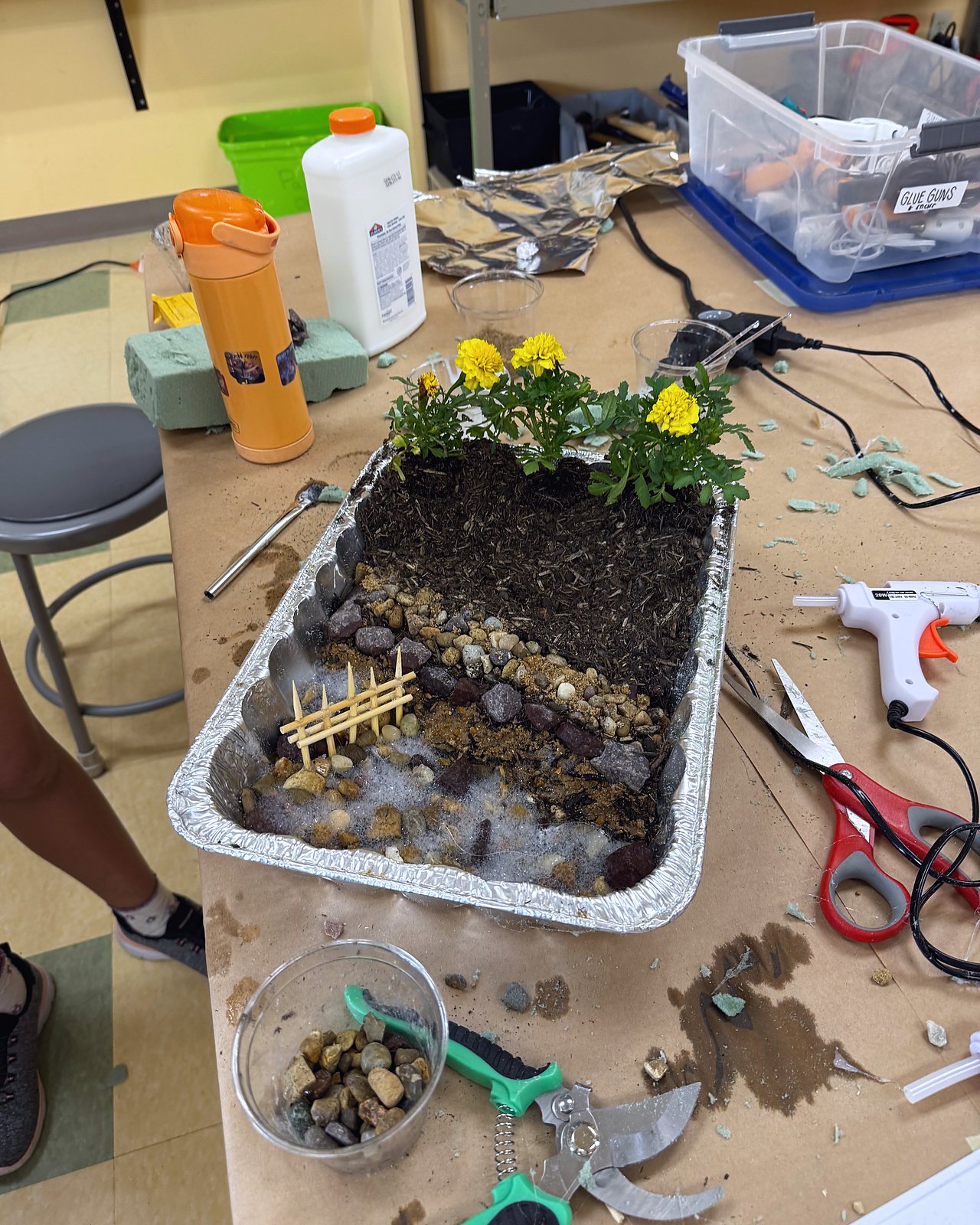 A habitat model built in a foil tray, with soil, stones, a fence and marigolds